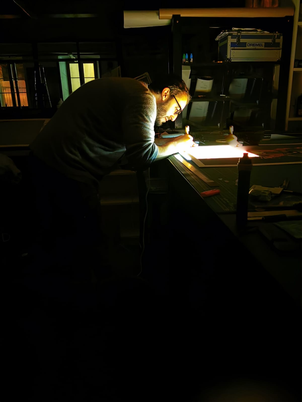 Artiste travaillant sur une œuvre dans son atelier, éclairé par une lumière de travail
