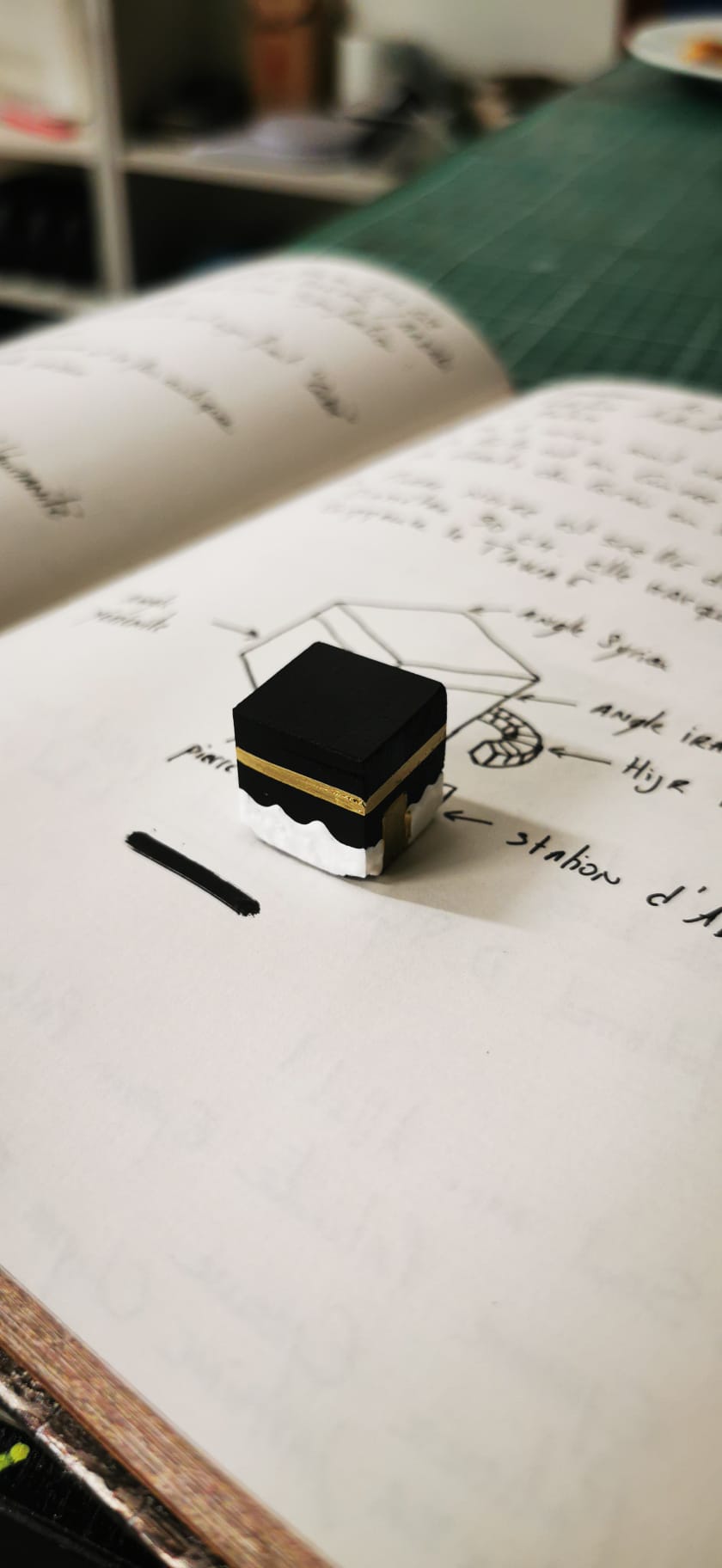 Maquette symbolique de la Kaaba posée sur un carnet de réflexion et de croquis
